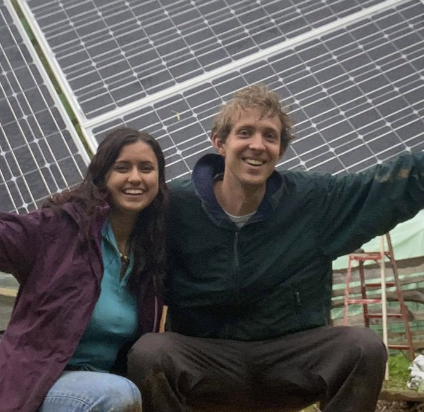 Odalys Benitez and leon santen smiling in front of several solar panels that adjust their angle with the sun's movement. 